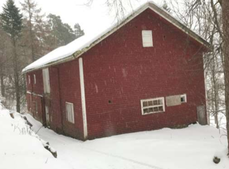Rød låve i hvitt vinterlandskap i skogen. Før restaurering startet. Låvebroa er helt borte. Furøya, Agder. Foto.